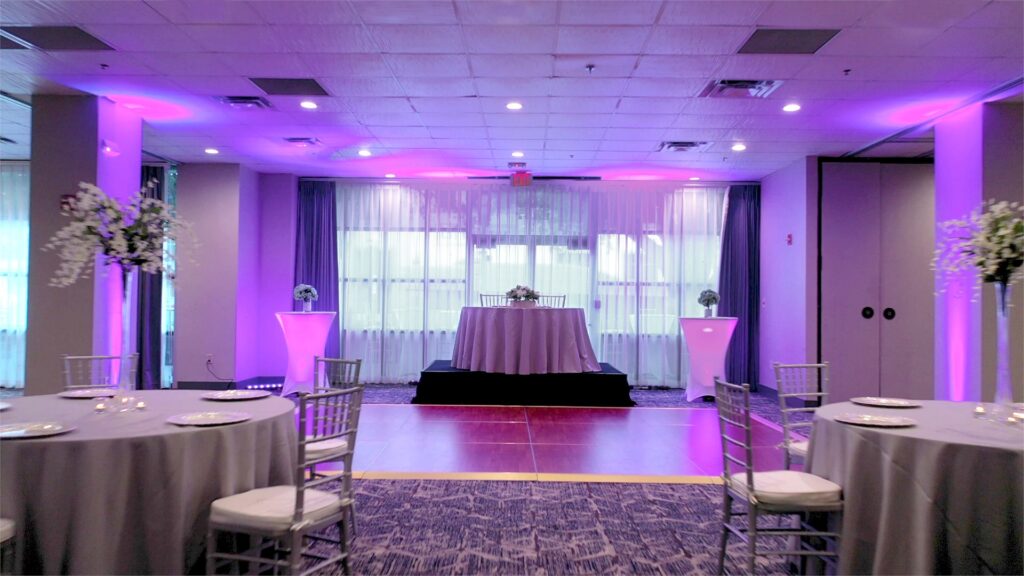 ballroom decorated for wedding reception with purple uplights and a sweetheart table placed on a raised platform